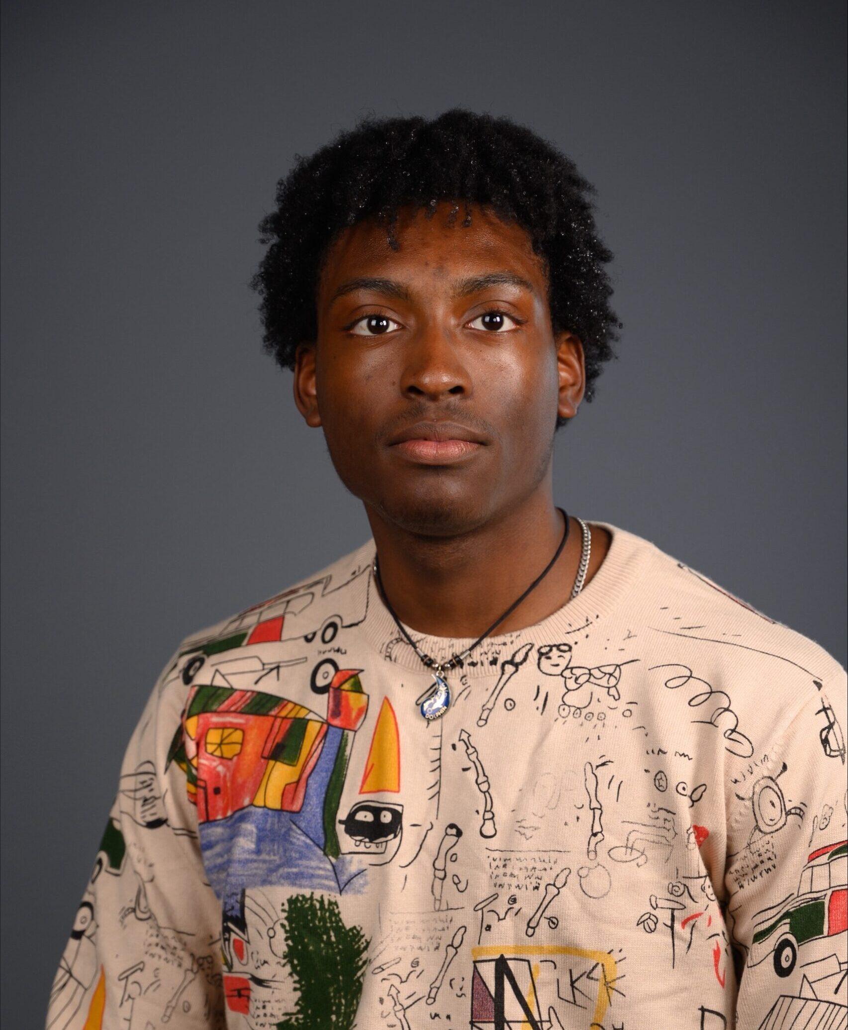 A young man wearing a tan, long sleeve shirt looks straight at the camera as he poses for a portrait photo.